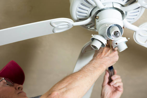Electrician repairing ceiling fan for neighbor. He replaced the motor for the fan. Blue collar Caucasian senior man is retired but is still active and enjoying doing small repairs for others. Helping neighbors.