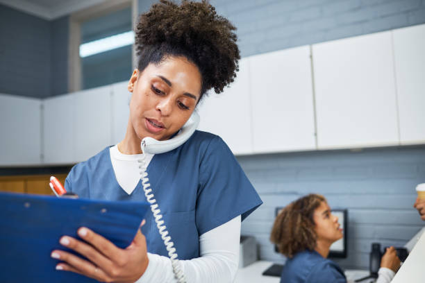 A female healthcare worker multitasks by speaking on the phone and writing notes in a modern medical office setting. She exudes professionalism, interaction, and communication in her administrative duties.