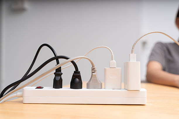 Close up of power strip with multiple plugs and tangled cables on wooden desk. Concept of electricity, energy supply, power connection, safety, and modern lifestyle with electronic devices at home.