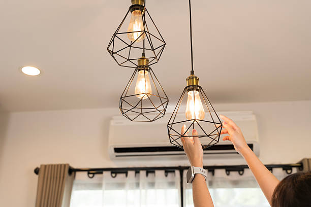The hands adjusting beautiful modern pendant lights in a stylish interior setting. Showing home improvement action and interior decoration concept in modern living space with stylish lighting design.