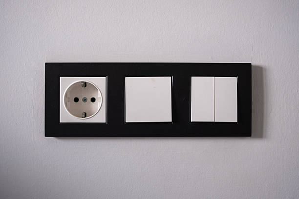 Minimalist modern electrical wall panel with power socket and light switches mounted on a white interior wall. Concept of home interior design, electricity, renovation, and smart home infrastructure.