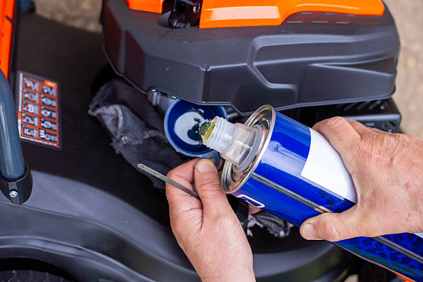 Hands pouring motor oil from a blue can into a lawnmower engine. machine maintenance, technical service, garden tool care.