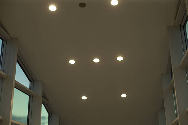 Clean ceiling dotted with recessed lights creating soft even illumination, neutral vents and sensors visible, calm institutional