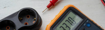 Multimeter and electric splitter on a white wooden background. Measurement of electric network parameters. Electrical safety. Qualified electrician services. Selective focus.