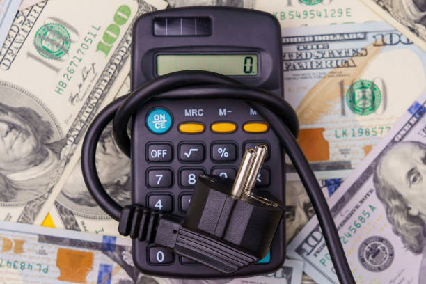 Plug from an extension cord tied in a knot on a blurred background of a calculator and dollars, selective focus. The concept of the energy crisis and electricity inflation. Rising electricity prices