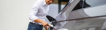 An attractive adult mixed male charging his luxurious electric car before leaving to go out on a date. He is located on a driveway in front of his home. His clothes are smart-casual. He is smiling and looks excited.