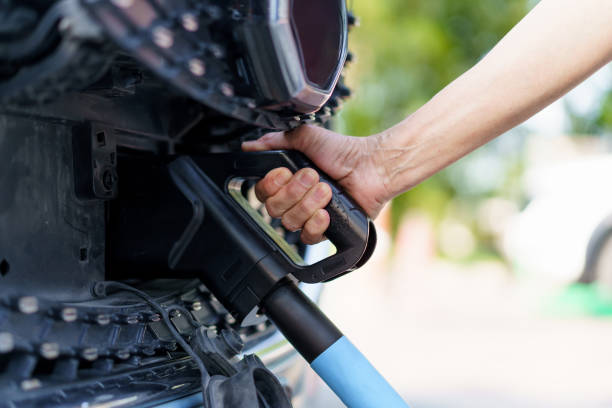 Unrecognizable Asian woman holding aa DC - CCS type 2 EV charging connector at EV charging station, woman preparing an EV - electric vehicle charging connector for recharge a vehicle.