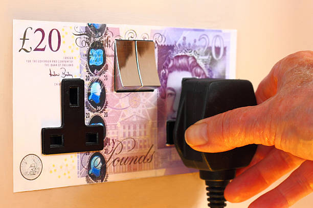 London, England - August 9, 2013: Concept photograph highlighting the high cost of electricity. An elderly lady is placing an electrical plug into a standard UK electrical wall socket. The backplate of the socket is a British A#20 note.